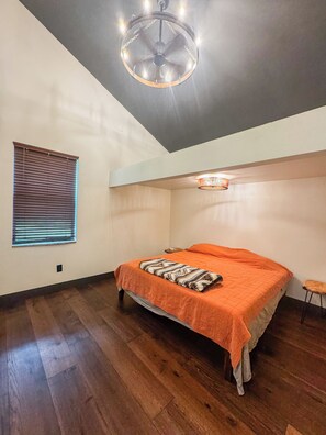 A bedroom with a bed, a ceiling fan, a window with blinds, and a small stool.
