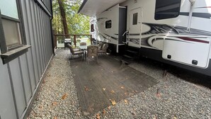 Et overdækket udendørsområde med grill, siddepladser og en stor campingvogn parkeret ved siden af en bygning.