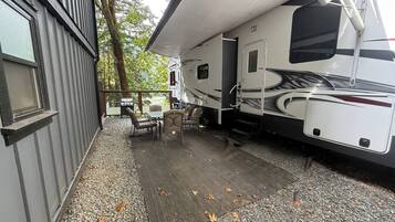 A covered outdoor area with a grill, seating, and a large RV parked adjacent to a building.