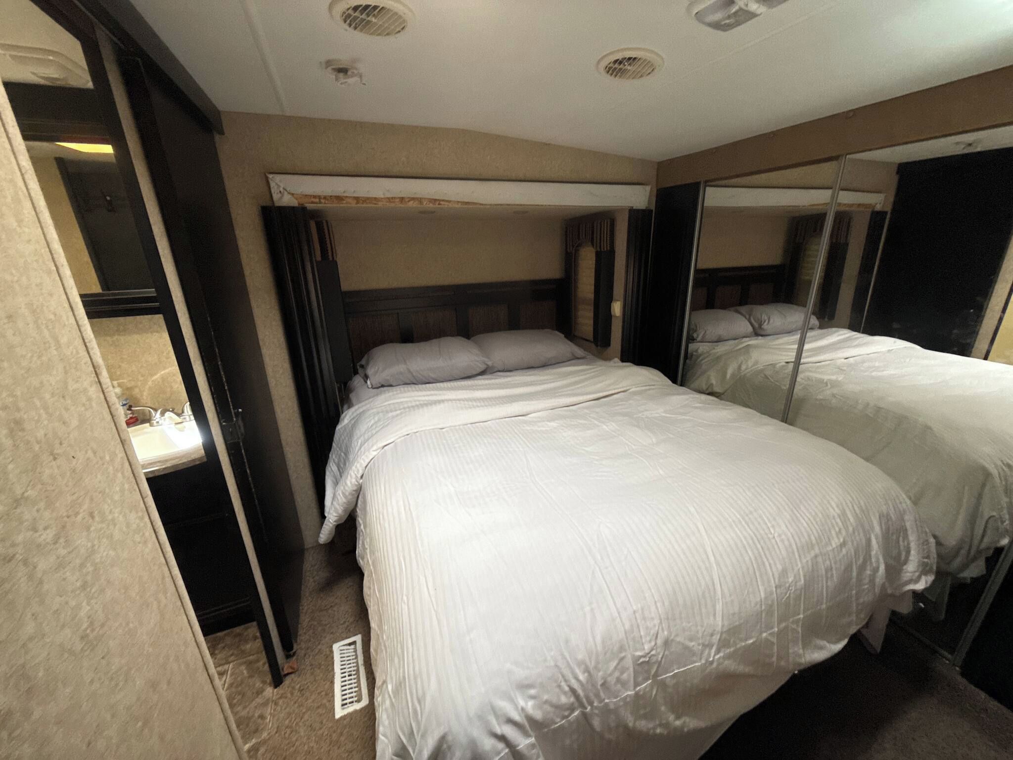 A hotel room with two beds, a mirror, a wardrobe, and a bathroom.