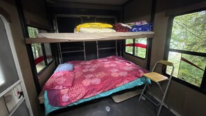 En rummelig indretning i en mindre autocamper med en køjeseng, et lille bord og et vindue med udsigt til grøn natur.