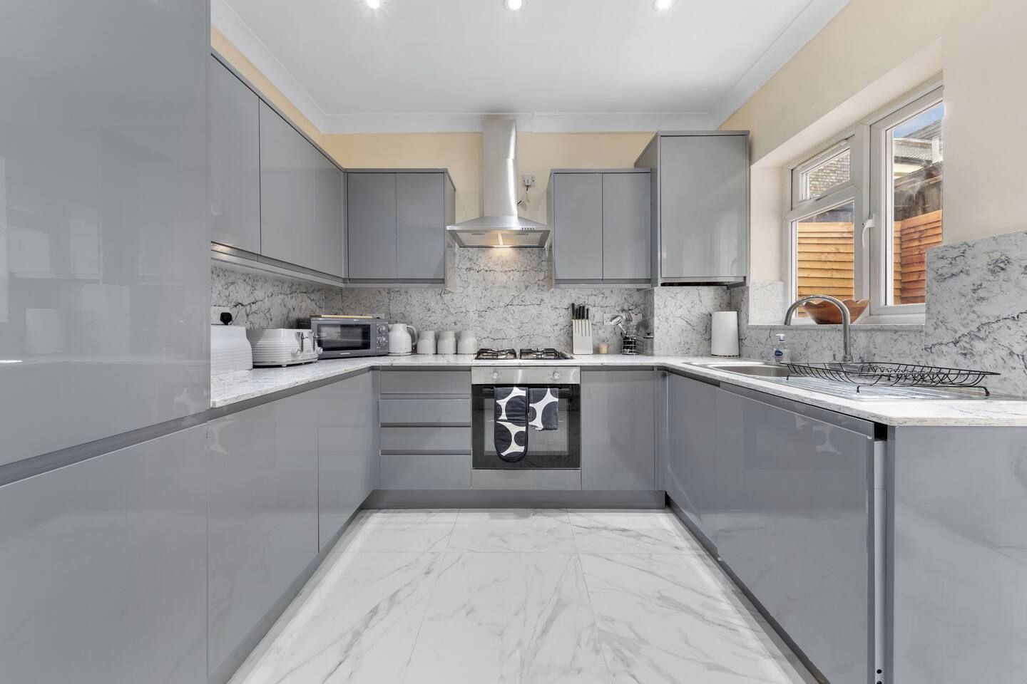 Una cucina moderna con mobili grigi, forno integrato e finestra con vista su un terrazza in legno.