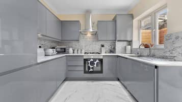 A modern kitchen with grey cabinets, a built-in oven, and a window overlooking a wooden deck.