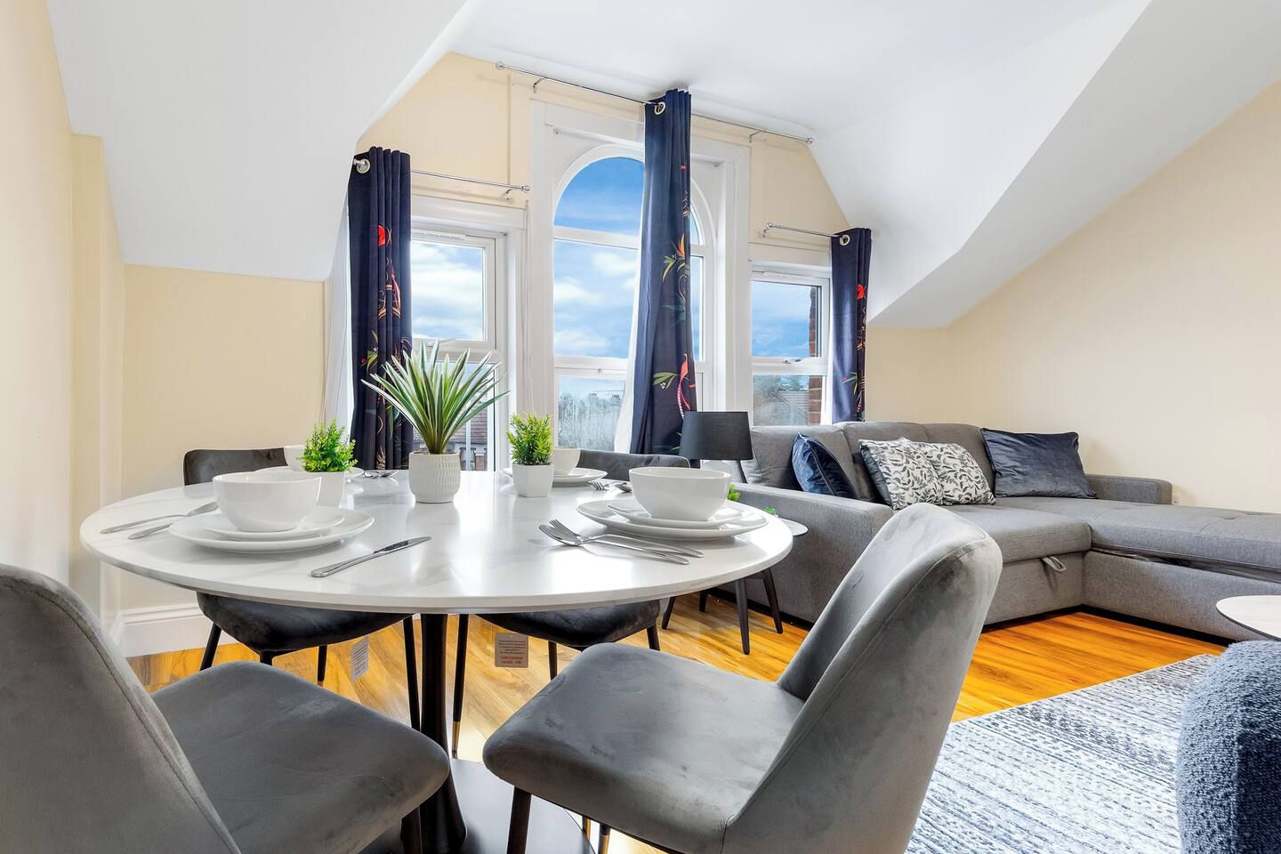 A modern living room with a dining area, grey sofas, and a round table set for four.