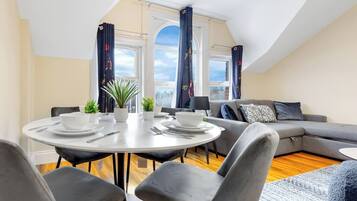 A modern living room with a dining area, grey sofas, and a round table set for four.