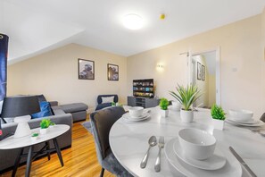 A modern living room with a dining area, grey sofas, a flat-screen TV, and a bookshelf. - Huge 9BR London Stay Perfect For Groups, Near Leytonstone Tube & Stratford! (Greater London)