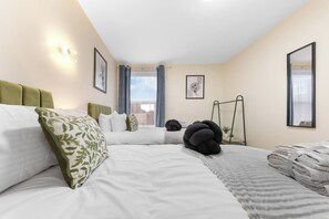 A hotel room with two beds, a large window with curtains, a wall-mounted lamp, and a framed picture. - Huge 9BR London Stay Perfect For Groups, Near Leytonstone Tube & Stratford! (Greater London)