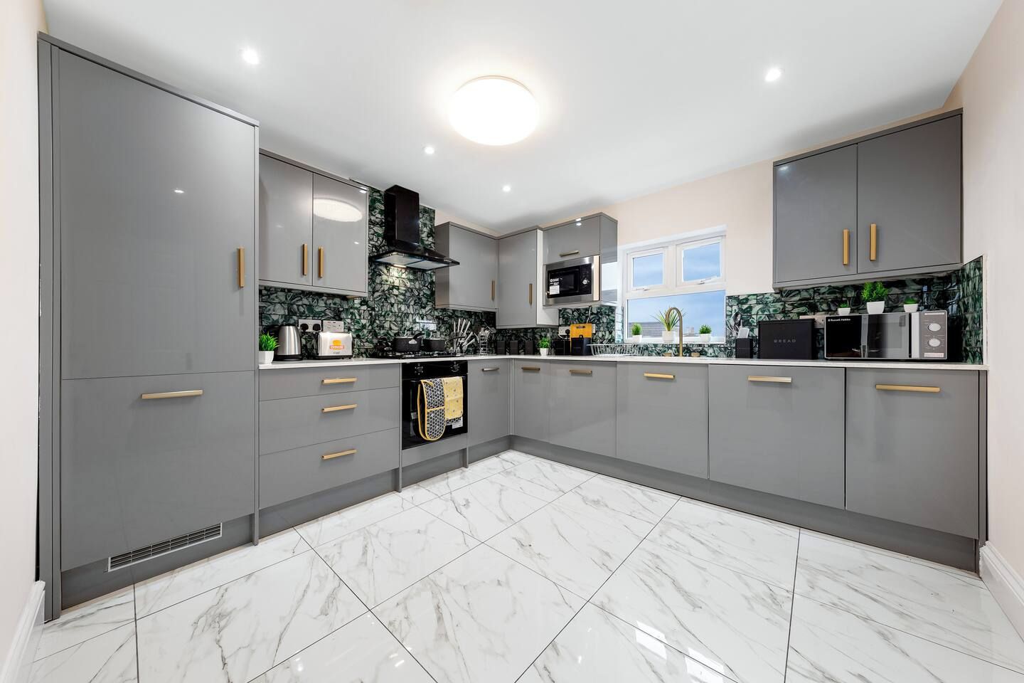 A modern kitchen with grey cabinets, a black microwave, and a tiled floor.