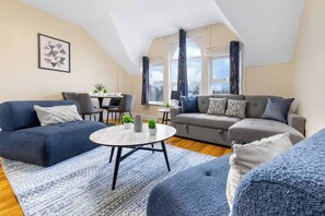 A modern living room with a sofa, a coffee table, and a dining area with chairs and a table. - Huge 9BR London Stay Perfect For Groups, Near Leytonstone Tube & Stratford! (Greater London)