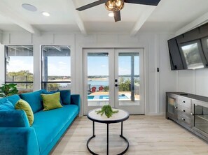 Ein modernes Wohnzimmer mit einem blauen Sofa, einem runden Couchtisch und Blick auf einen Pool durch Glastüren.