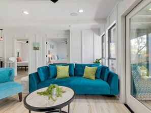 Ein modernes Wohnzimmer mit einem türkisfarbenen Sofa, einem runden Couchtisch mit Pflanze und einem großen Fenster mit Aussicht.
