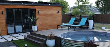 Un área de piscina moderna al aire libre con terraza de madera, sillas de descanso y plantas en macetas.