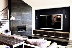 Ein modernes Wohnzimmer mit Kamin, großem Flachbildfernseher und einer Treppe.