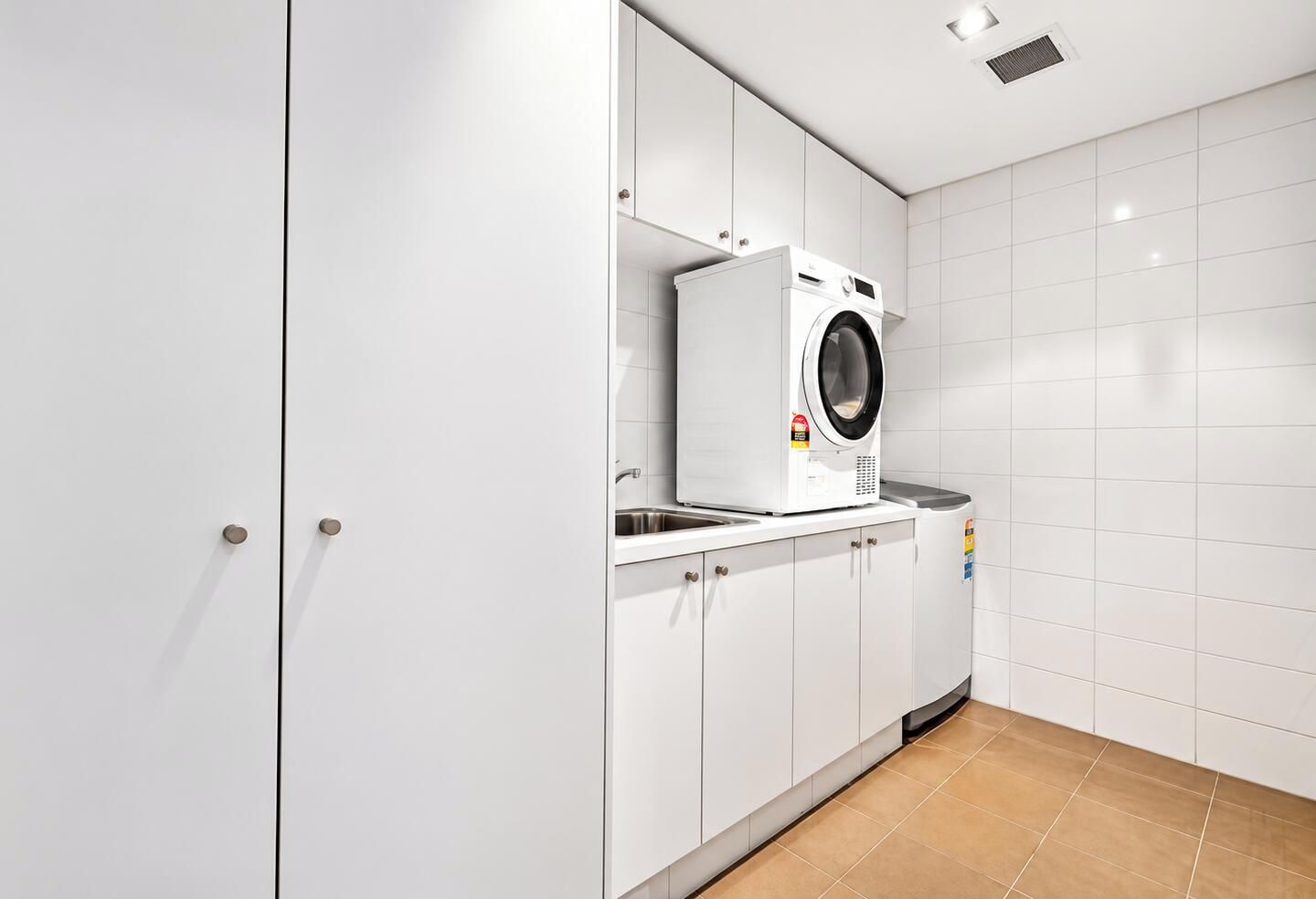 A modern laundry room with a front-loading washing machine, cabinets, and a tiled floor.