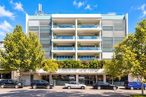 Un edificio de varios pisos con fachada plana, amplias ventanas y un estacionamiento al frente.