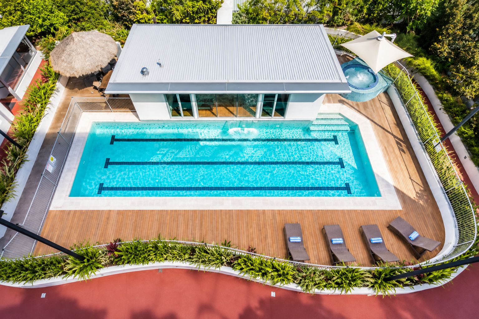 Ein moderner Swimmingpool mit einer Holzterrasse, Liegestühlen und einem Reetdachschirm.