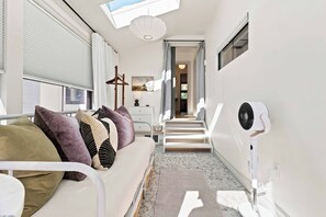 Ein schmaler Flur mit einem Bett, einem Ventilator und einer Treppe zu einem anderen Raum.