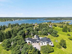Ein großes Haus, umgeben von dichtem Wald und einem See.