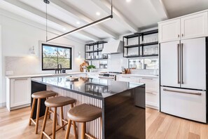 Una cucina moderna con isola centrale, sgabelli da bar, frigorifero e scaffali a incasso.