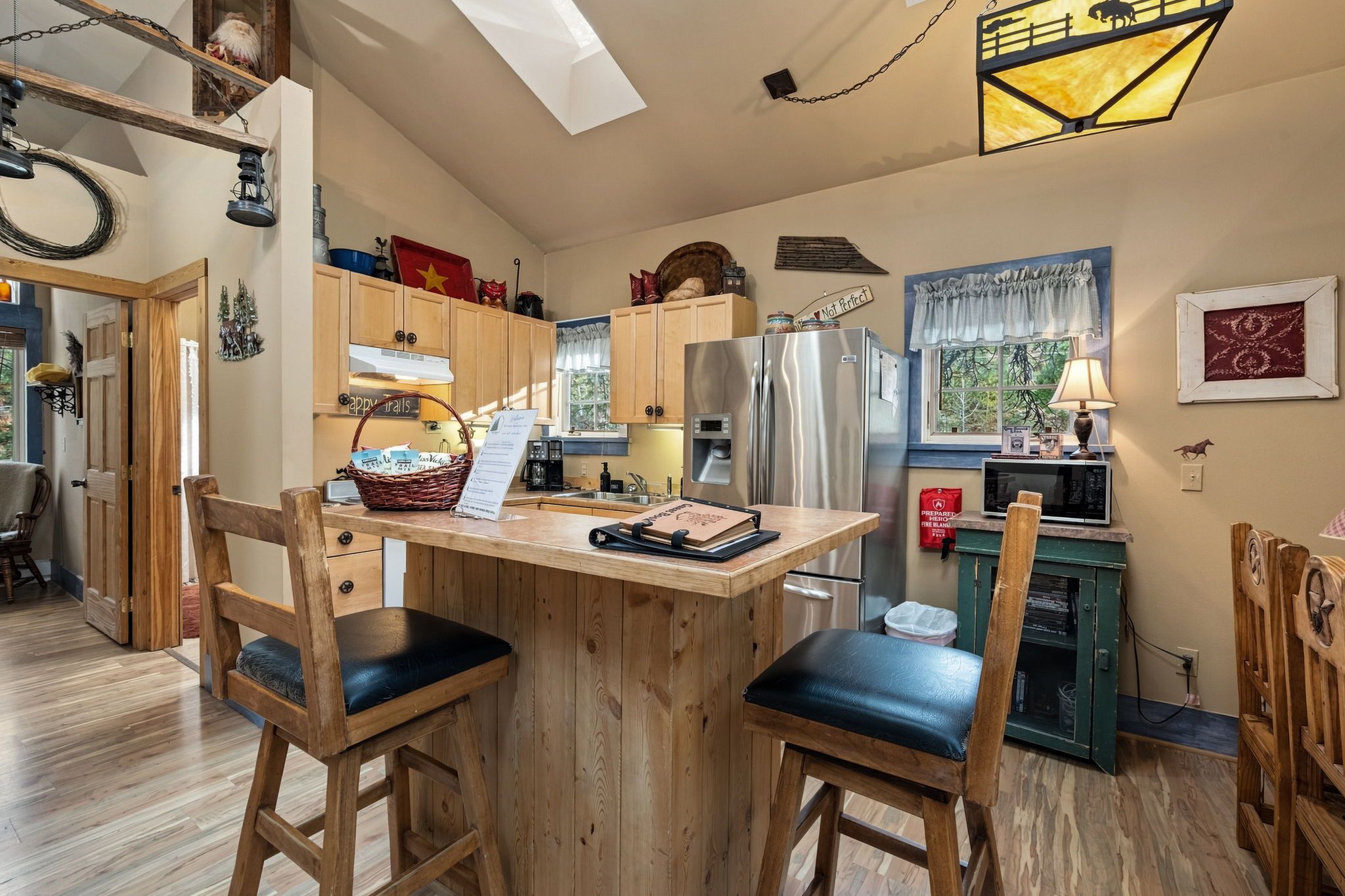 A kitchen with wooden cabinets, a stainless steel refrigerator, a wooden island with chairs, and a hanging light fixture.