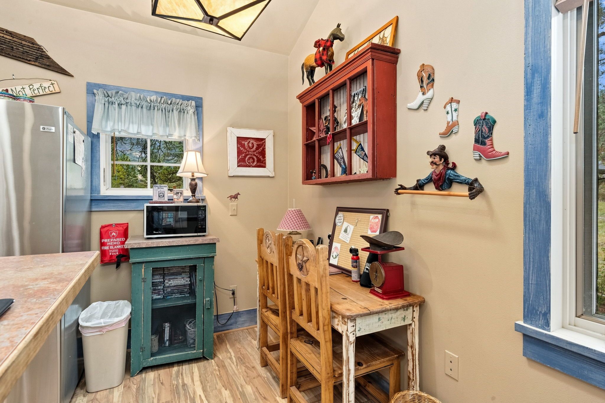 A kitchen with a microwave, a fire blanket, a wooden chair, and a window with a view.