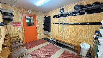 A room with a wooden wall, a red door, a bench, a trash bin, and shelves with helmets.