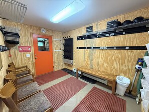 Une pièce avec un mur en bois, une porte rouge, un banc, une poubelle et des étagères remplies de casques.