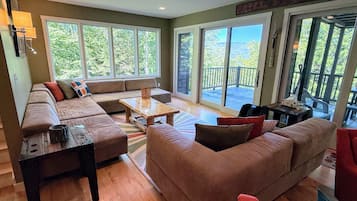A spacious living room with a large sofa, a coffee table, and a view through large sliding glass doors to an outdoor deck.