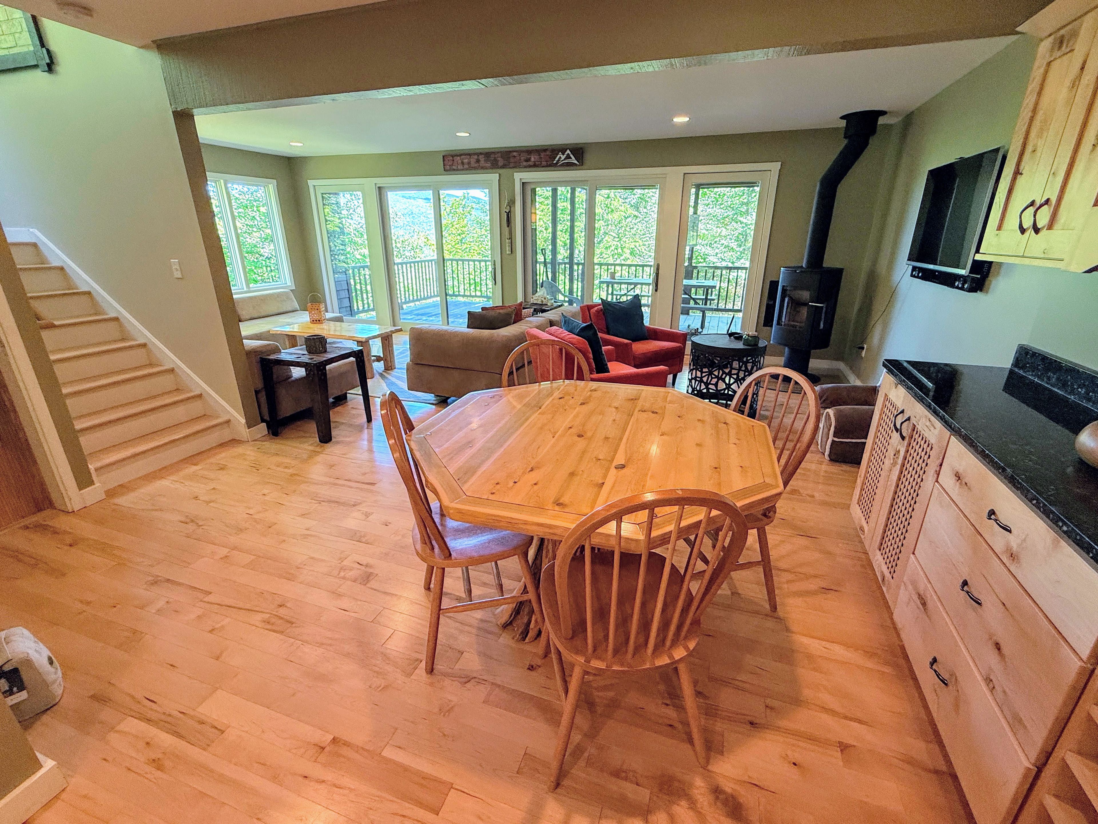 A spacious living area with a wooden dining table, chairs, and a kitchen with wooden cabinets and a black countertop.