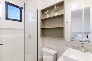 Ein modernes Badezimmer mit Toilette, Waschbecken und einer gläsernen Duschkabine. Über der Toilette befinden sich Regale mit Dekorationselementen.