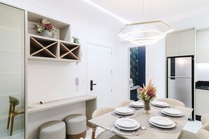 A modern dining area with a white table set for four, a built-in shelf with decorative items, and a refrigerator in the background. - Apt. w/ Balcony & Sea View 680m Beach Alx1601 (Itapema)