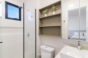 A modern bathroom with a toilet, sink, and a glass-enclosed shower. There are shelves above the toilet with decorative items. - Apt. w/ Balcony & Sea View 680m Beach Alx1601 (Itapema)