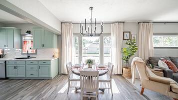 A spacious kitchen with light green cabinets, a dining area with a table set for four, and a living area with a sofa and a plant.
