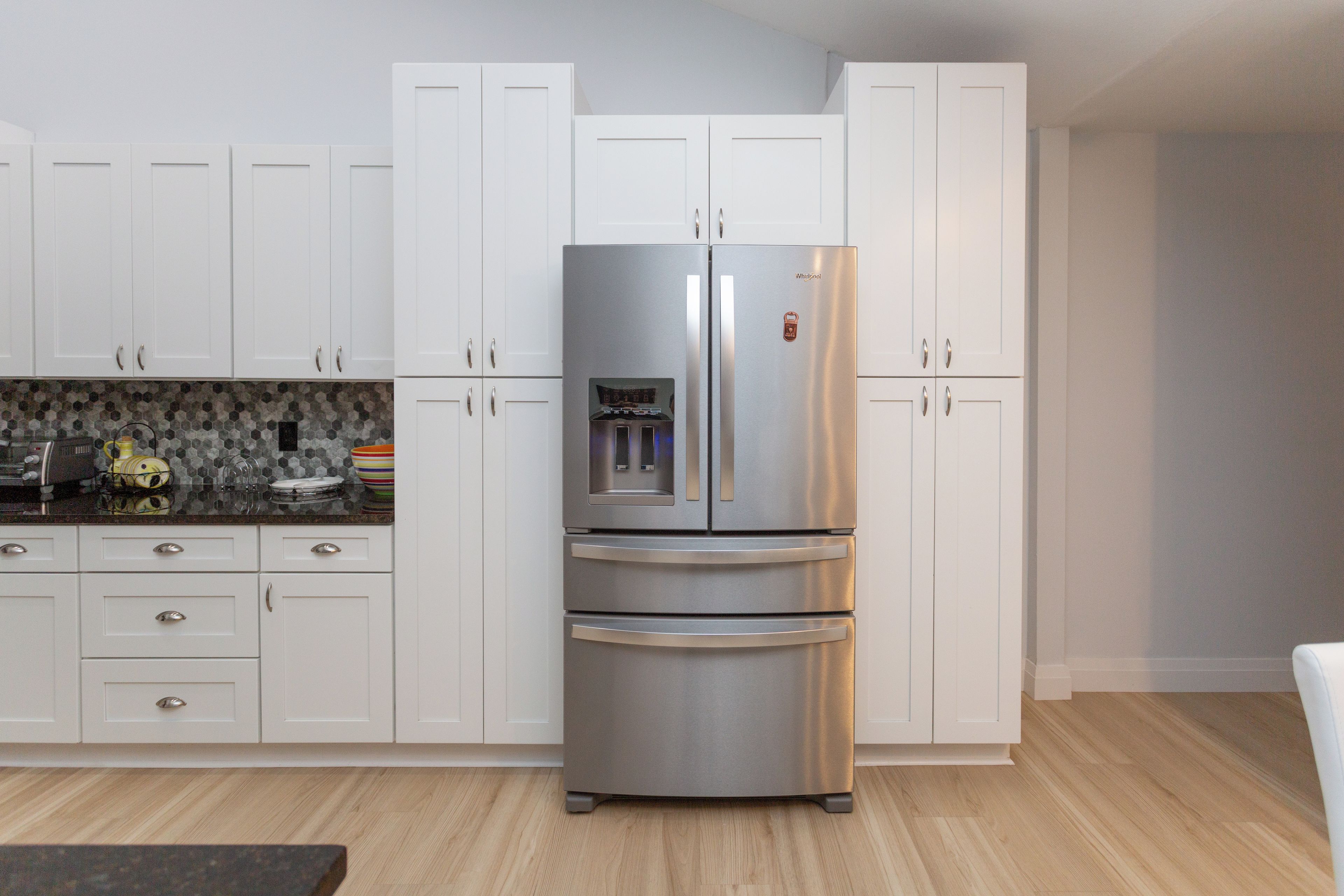 A kitchen with white cabinets, a stainless steel refrigerator, and a tiled backsplash.