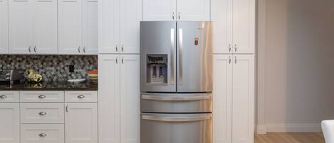 A kitchen with white cabinets, a stainless steel refrigerator, and a tiled backsplash.