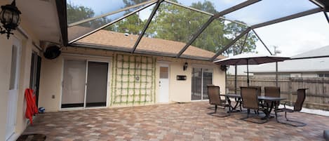 A covered patio area with brick flooring, outdoor furniture, and a view of the surrounding area.