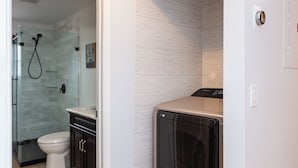 A modern bathroom with a glass shower enclosure, a toilet, and a built-in washer-dryer unit. - Wonderful 3-bedroom townhome with AC in peaceful Wellington (Wellington)