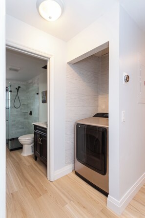 Une salle de bain moderne dotée d’une douche à parois de verre, de toilettes et d’un appareil combiné lave-linge et sèche-linge intégré.