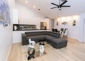 Un salon moderne avec un canapé d’angle, une table basse en verre et un ventilateur de plafond.