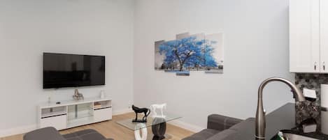 Un salon moderne doté d’un téléviseur à écran plat, d’une table basse, d’un canapé et d’un coin repas comprenant un comptoir de cuisine et un évier.