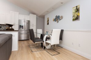 Une cuisine moderne avec des meubles blancs, un réfrigérateur en acier inoxydable et un coin repas comprenant une table et des chaises en verre.