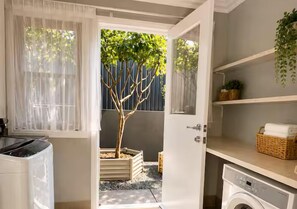 A laundry room with a washing machine, a dryer, and a small tree in a planter. - Large Stylish Home near CBD - Sleep 10 (Coorparoo)