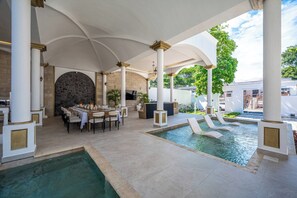 Ein überdachter Außenbereich mit Pool, Sitzgelegenheiten und einer Steinmauer.
