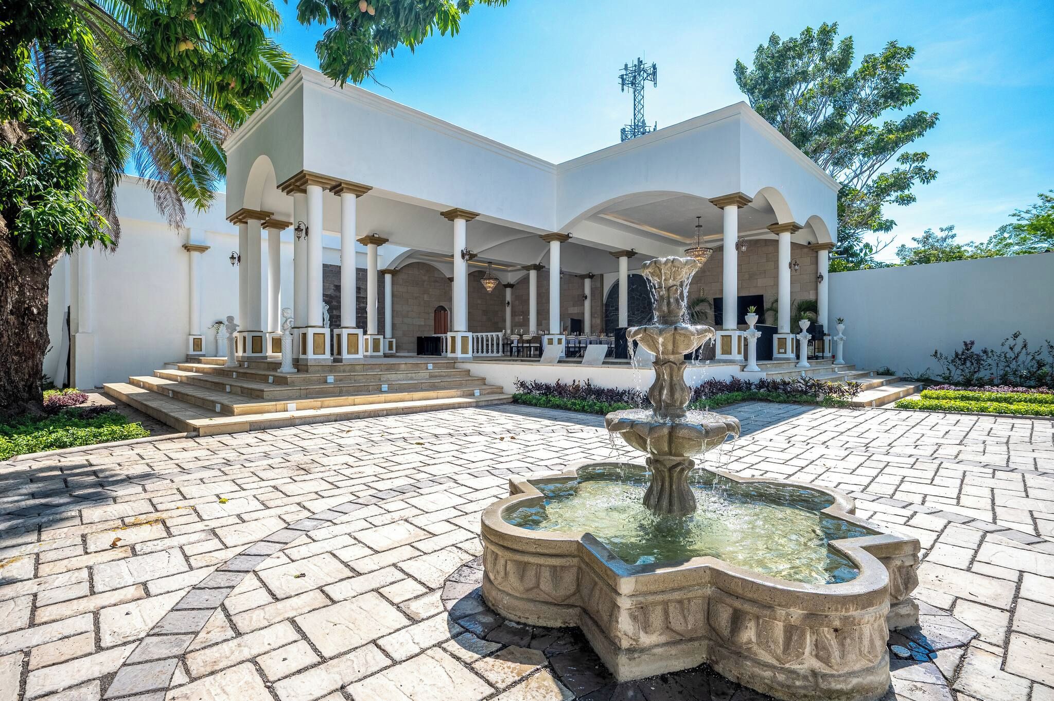 A building with a fountain, steps leading to a covered entrance, and a clear sky.