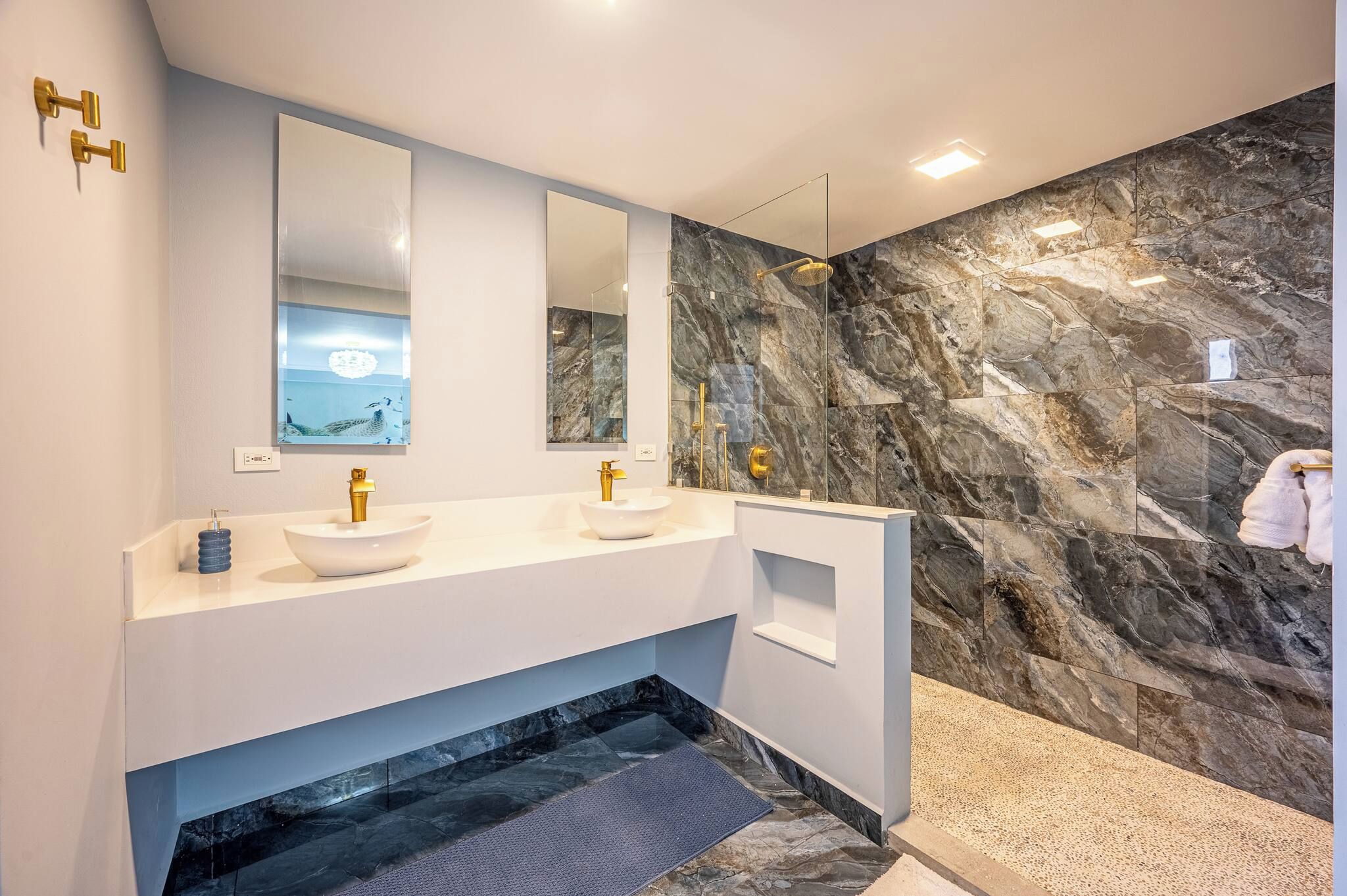 A modern bathroom with two sinks, a large mirror, and a marble wall.