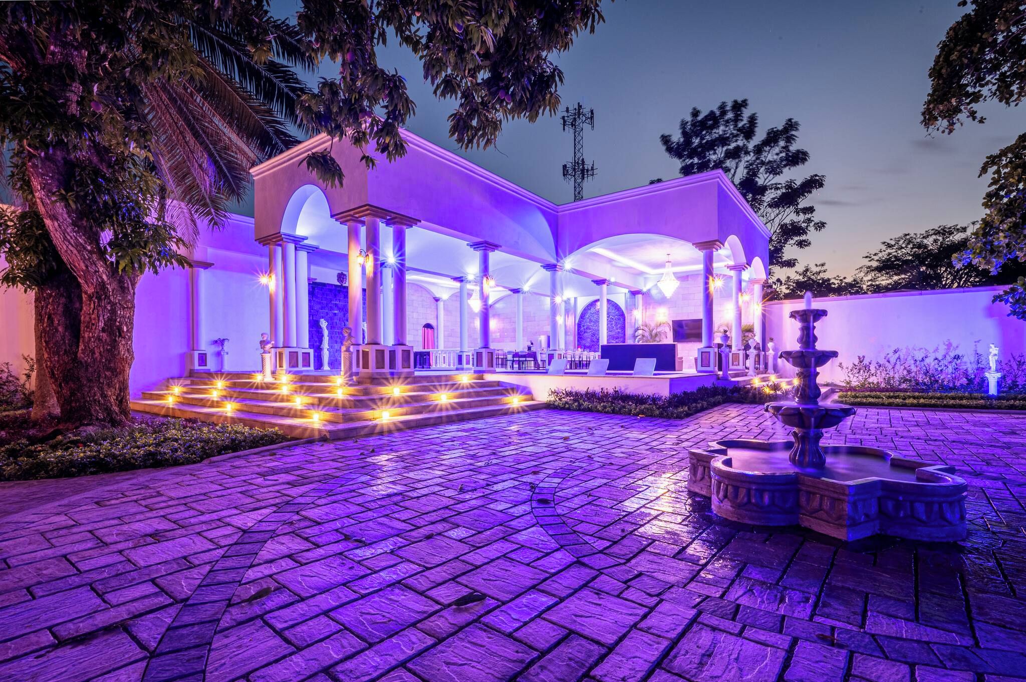 A hotel with a covered outdoor area, a fountain, and a stone-paved entrance.