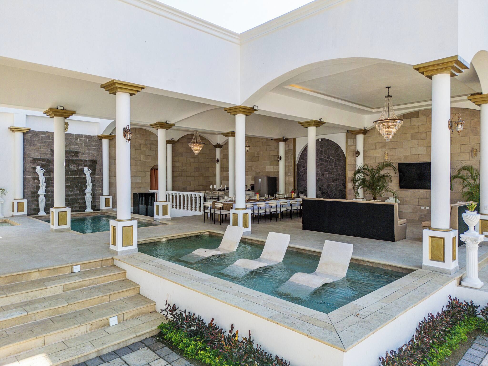 Un área de piscina interior amplia con múltiples sillones, un bar y una zona de estar con mesas.