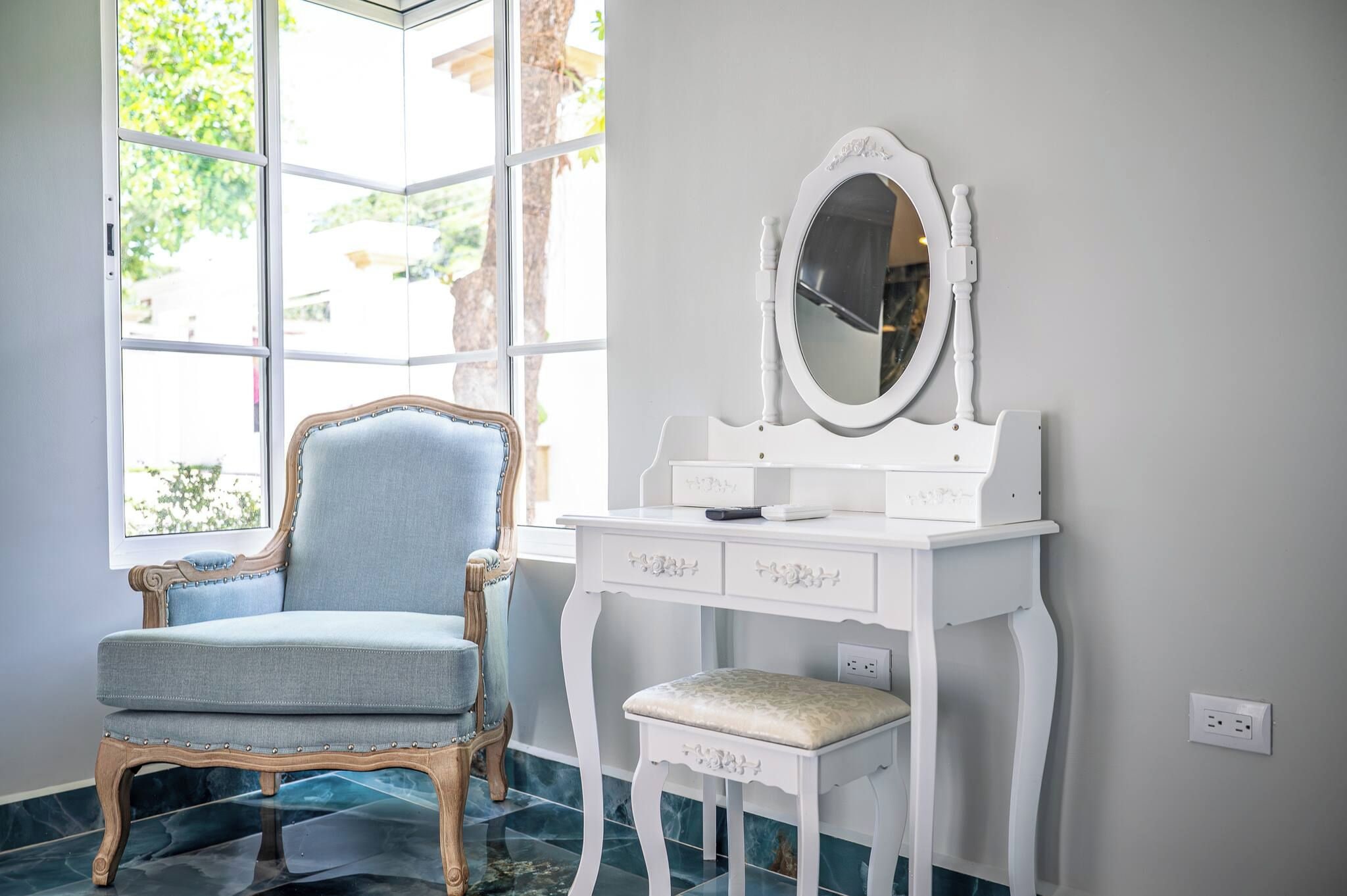 A room with a vanity table, a chair, and a large window.