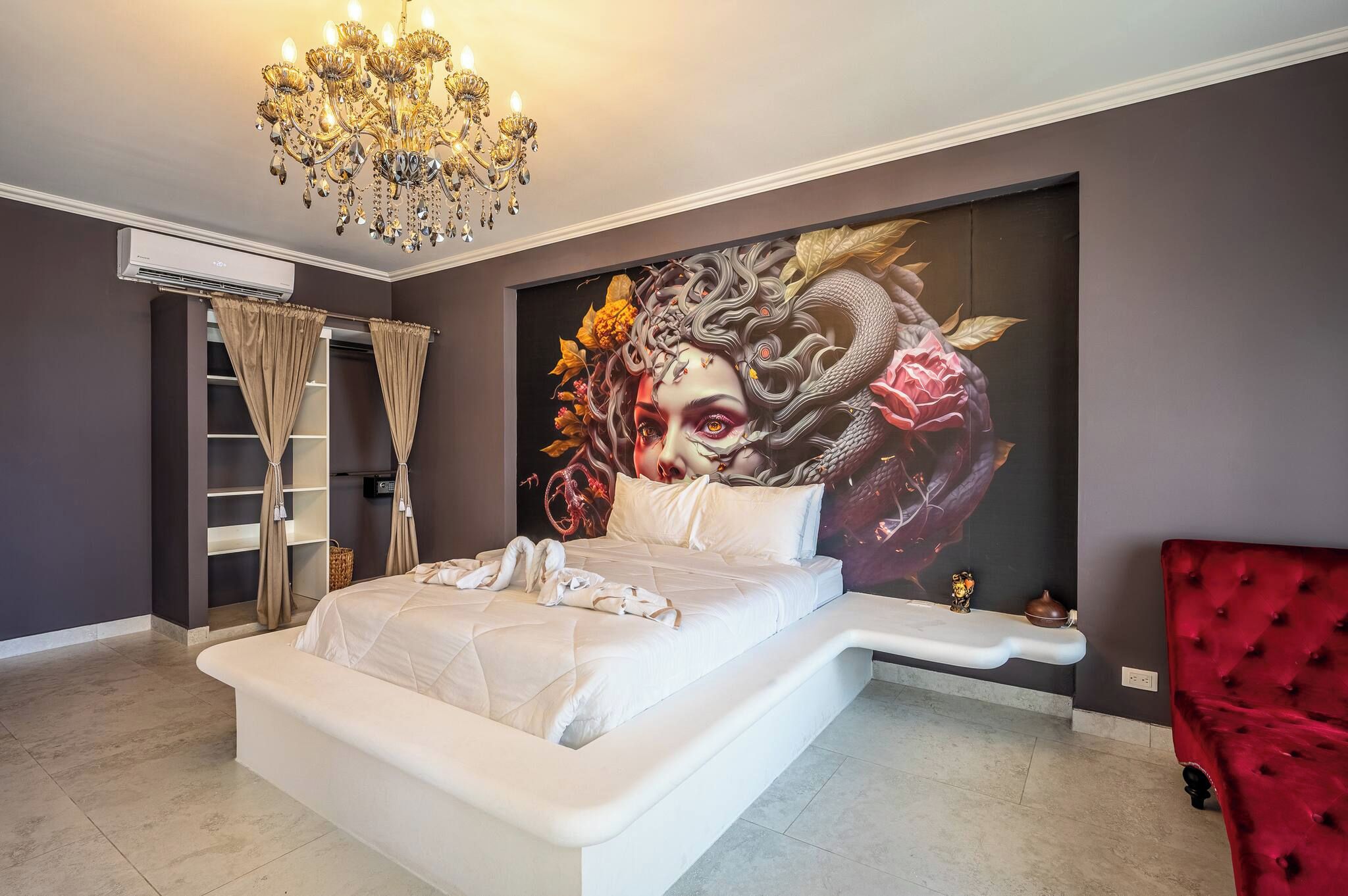 Un dormitorio con una cama grande, una silla roja, una araña y un mural en la pared.