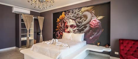 Un dormitorio con una cama grande, una silla roja, una araña y un mural en la pared.